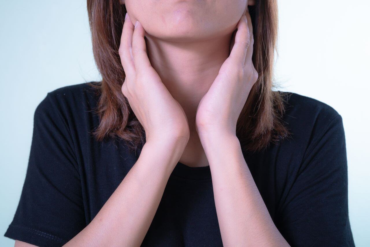 Woman in a black T-shirt pressing both hands to the sides of her neck, just below the jaw